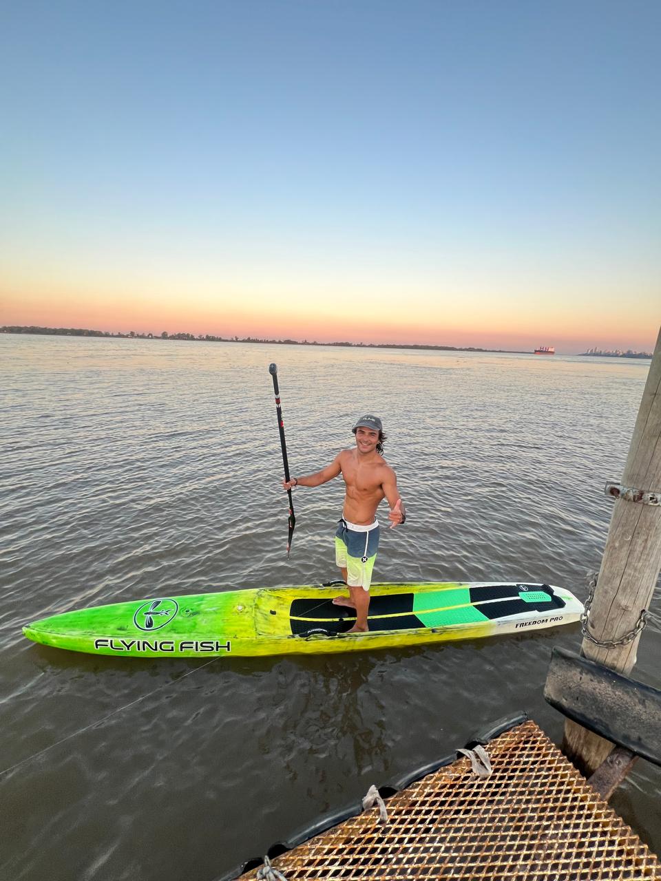 Santino parado sobre su tabla Flying Fish al atardecer